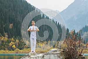 A young man in white practices yoga in the mountains. Pose Samasthiti namaskar