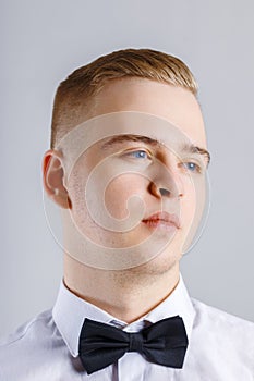 Young man in white shirt and black bow tie poses in studio