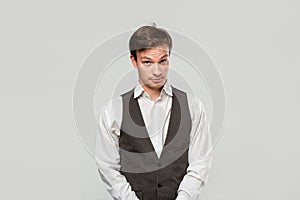 Young man in a white shirt and grey vest in high dudgeon over grey background