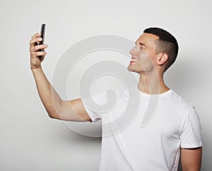 Young man in white shirt holding mobile phone and making photo of himself