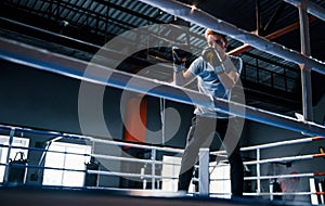 Young man in white shirt and protective gloves doing exercises in boxing ring