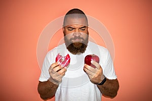 Young man with white t-shirt and big beard making difficult choice between red apple and pink donut