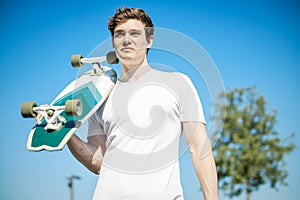 Young man in white T-shirt holding longboard or skateboard in the skatepark.