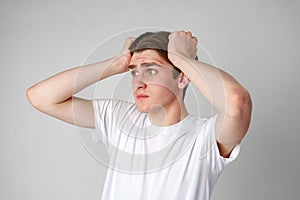 Young Man In White T-Shirt Looking Worried With Hands On Head Against Plain Background