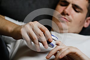 A young man in a white T-shirt is sick with COVID-19 coronavirus and measures oxygen saturation at home on the couch