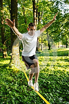 Young man in white tshirt and shorts on the rope keeping balance