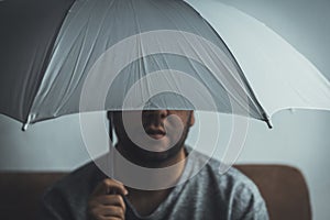 Young man with white umbrella sitting on a sofa at home - Safety concept - not take risks concept