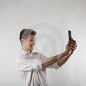 Young man in white using smartphone. Man taking selfie over bright background