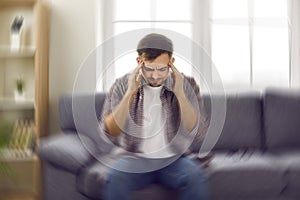 Young man who feels dizzy and has spinning vertigo sensation is sitting on sofa at home