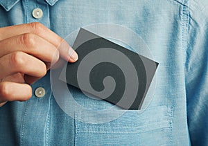 Young man who takes out black blank business card from the pocket of his shirt