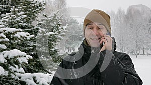 A young man in winter forest talking on the phone. Big snowfall. He admires the sides of snow and trees. A man in a dark