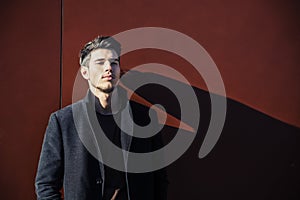 Young Man in a Winter Outfit Leaning on Red Wall