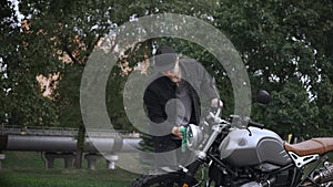 Young man wiping his leather scrambler motorbike with cloth on the street