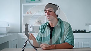 Young man in wireless headphones is talking on a video call using his mobile phone. Popular blogger is recording a video