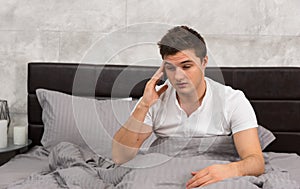 Young man woke up with hangover sitting in stylish bed with grey