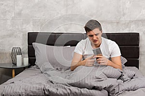 Young man woke up and looking at his mobile phone while sitting