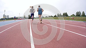 Young man and woman athletes are running in front of the camera at athletics track during a day training in slow motion