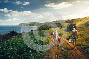 Young Man and Woman with Backpack, view from behind, Walking along the Road Towards the Sea Adventure Travel Relax Concept