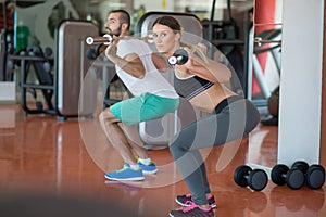 Young man and woman with barbell flexing muscles and making shoulder press squat in gym