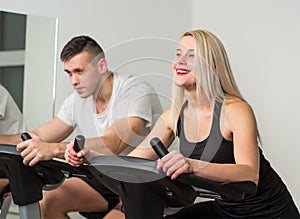 Young man and woman biking in the gym, exercising legs doing cardio workout cycling bikes