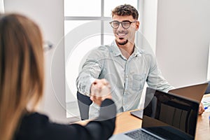 Young man and woman business workers shake hands working at office