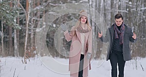 A young man and a woman in a coat are having fun and playing with snow in a winter forest in slow motion. Happiness and