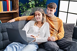 Young man and woman couple using laptop sitting on sofa at home