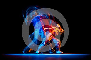 Young man and woman dancing hip-hop in sportive style clothes on dark background at dance hall in mixed neon light