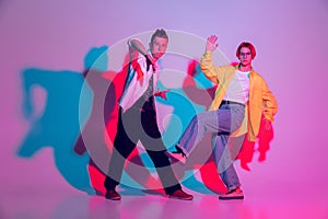 Young man and woman dancing hip-hop, street style isolated on studio background in neon light