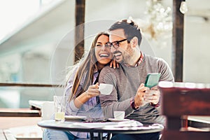 Young man and woman dating and spending time together in cafe, using phone