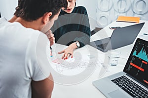 Young man and woman designer sketching a construction project at laptop and drawing plan while working at office