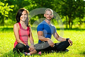 Young man and woman doing yoga in the sunny summer park