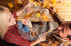 Young Man And Woman Eating Fast Food Potato Sitting At Wooden Table In Cafe Top Angle View