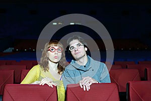 Young man and woman in glasses watch movie and surprise