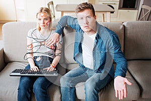 Young man and woman have social media addiction. Sitting on sofa. Hostages. Emotionless woman on sofa. Worried man