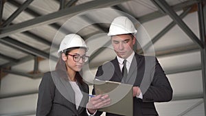 Young man and woman in helmets with documents at a construction site. Bosses in suits are discussing an architecture