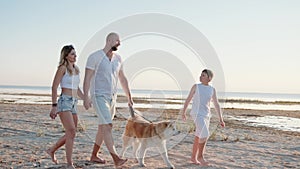 Young man and woman holding hands, walking with boy and dog on the beach