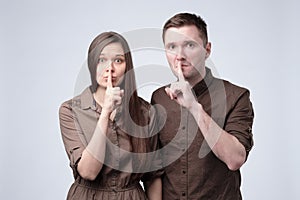 Young man and woman holding their fingers on lips asking to be silent