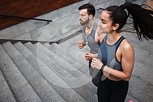 Young man and woman are jogging. They are going up by steps. The couple is looking straight. They are concentrated on