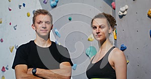 Young man and woman looking into the camera standing in front of climbing wall