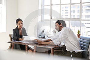 Young man and woman looking at documents across office desks