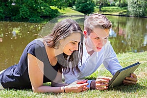 Young man and woman lying at water reading Ipad