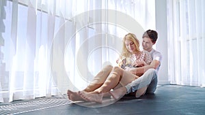 Young man and woman in pajamas sit on floor and pat domestic bunny on her lap