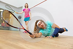 Young man and woman playing squash, focus on male hitting ball