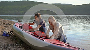 Young man and woman prepare their inflatable kayak for paddling in a lake or sea. Slowmotion shot