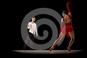 Young man and woman, professional dancers, performing, dancing tango, ballroom over black background under spotlight