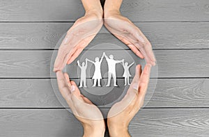 Young man and woman protecting paper family figure with their hands on grey wooden background photo