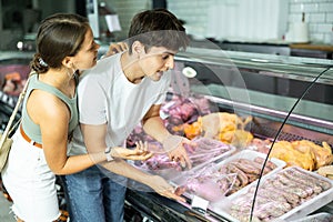 Young man and woman purchasers buying sausages in butcher shop