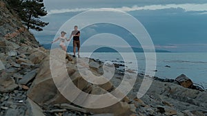 Young man and woman running along seashore on summer evening outdoors.