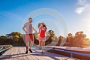 Young man and woman running along summer river dock. Couple having fun at sunset. Guys relaxing